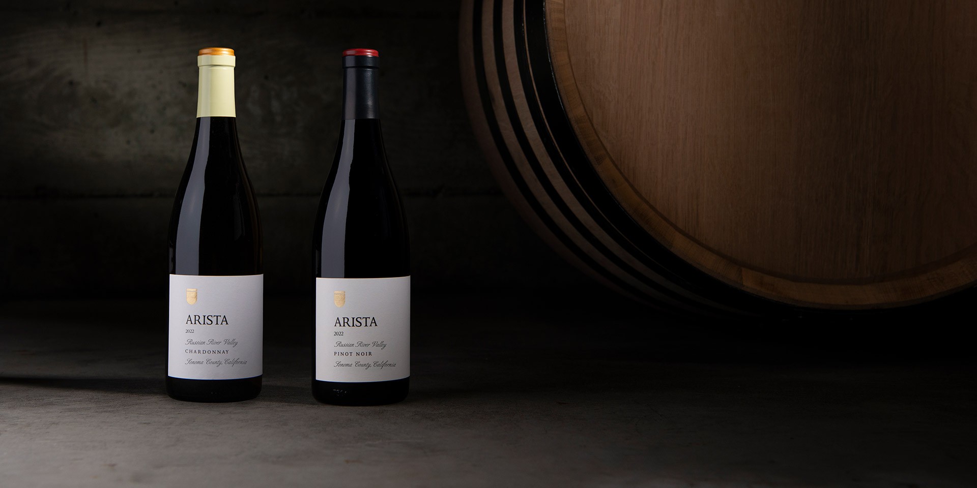 Two bottles of Arista wine with a wine barrel in the background